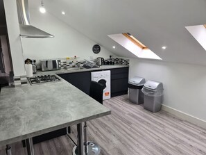 A modern kitchen with a gas stove, a washing machine, and two trash bins. - SAV Stays 2 Bed Flat, Saffron Leicester-1st Floor (Leicester)