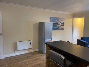 A compact kitchen with a refrigerator, a built-in oven, and a small dining area with a table and chairs. - SAV 1-Bed Flat, Walking Distance to Watford Centre (Hertfordshire)