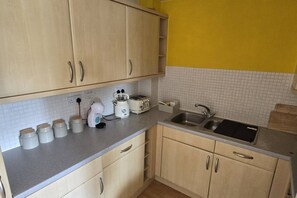 A kitchen with light wooden cabinets, a white countertop, a sink, and a yellow wall. - SAV 2-Bed Flat, Uxbridge (Greater London)