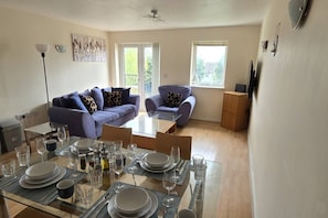 A modern living room with a glass dining table set for a meal, two sofas, and a ceiling fan. - SAV 2-Bed Flat, Uxbridge (Greater London)