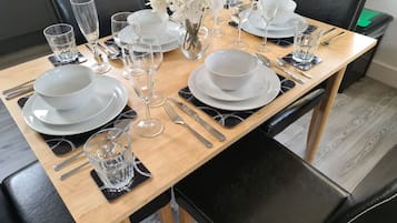 A dining table set with white plates, glasses, and cutlery, accompanied by a vase of white flowers.