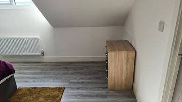 A room with a sloped ceiling, a radiator, a wooden cabinet, and a brown rug.