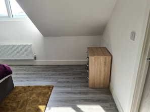 A room with a sloped ceiling, a radiator, a wooden cabinet, and a brown rug.