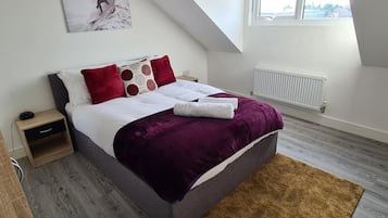 A bedroom with a bed, a nightstand, a window, and a radiator.
