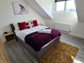 A bedroom with a bed, a nightstand, a window, and a radiator.