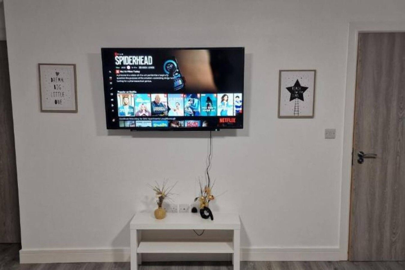 Un téléviseur à écran plat fixé au mur, au-dessus d’une console blanche agrémentée d’objets décoratifs.