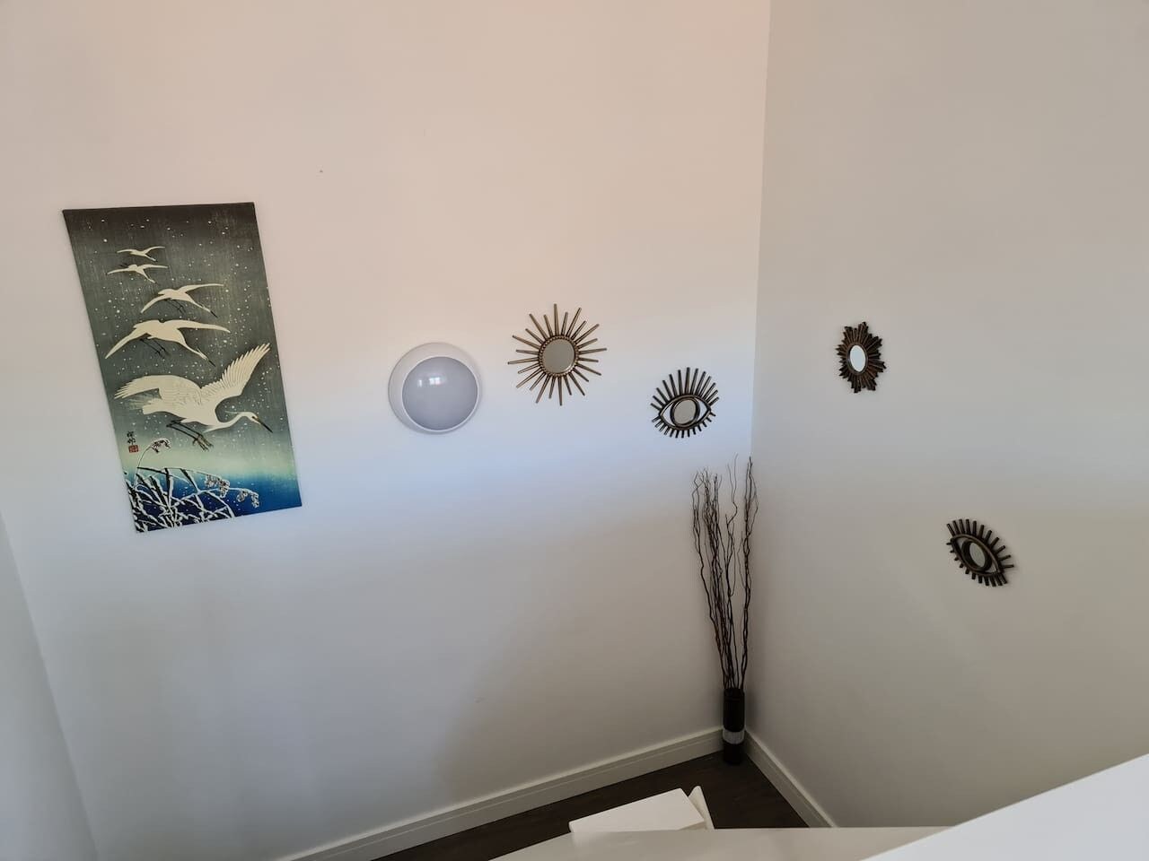 A room with a wall-mounted artwork of birds, a round light fixture, and several wall decorations including sunburst and eye motifs.