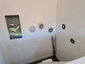 A room with a wall-mounted artwork of birds, a round light fixture, and several wall decorations including sunburst and eye motifs.