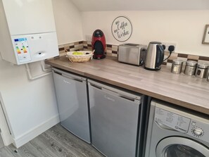 A compact kitchen with a dishwasher, a washing machine, a toaster, and a kettle.