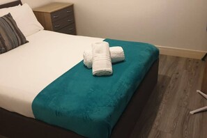 Ein Bett mit einer türkisblauen Tagesdecke und zwei aufgerollten weißen Handtüchern.