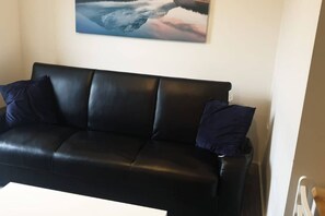 Ein schwarzes Ledersofa mit zwei Kissen vor einer Wand mit einem Gemälde.