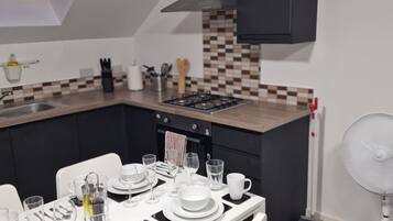 A modern kitchen with a dining area set for four, featuring a gas stove, a sink, and a fan.