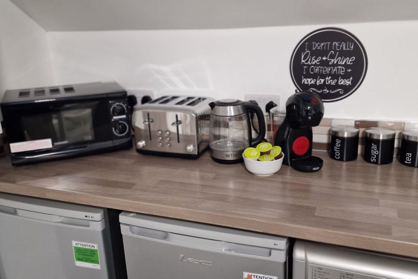 A kitchen counter with a microwave, toaster, coffee maker, and labeled containers for coffee, sugar, and tea.