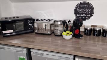 A kitchen counter with a microwave, toaster, coffee maker, and labeled containers for coffee, sugar, and tea.