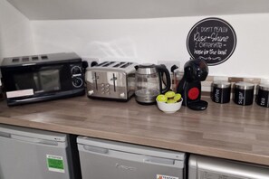 Eine Küchenarbeitsfläche mit Mikrowelle, Toaster, Kaffeemaschine und beschrifteten Behältern für Kaffee, Zucker und Tee.