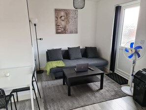 Una sala de estar moderna con un sofá gris, una mesa de centro con una computadora portátil, un ventilador de pie y una lámpara de pie.