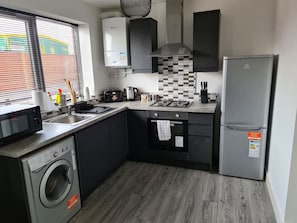 A compact kitchen with a washing machine, a refrigerator, a microwave, a gas stove, and a tiled backsplash. - Sav Stays Apartments Nottingham Road - 1 Bed Flat (Leicestershire)