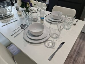 A dining table set with white plates, bowls, cutlery, and glasses, with a salt and pepper shaker on the table. - Sav Stays Saffron Leicester-2 Bed Flat (Leicester)
