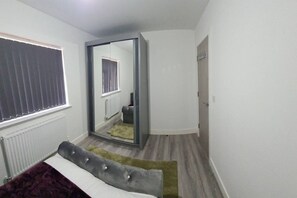 Ein Schlafzimmer mit einem Bett, einem großen Spiegel, einer Heizung und einer Tür zu einem anderen Raum.