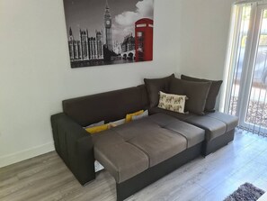 Ein modernes Wohnzimmer mit einer Couch, einem Gemälde von Londoner Sehenswürdigkeiten und Blick durch eine Glastür.