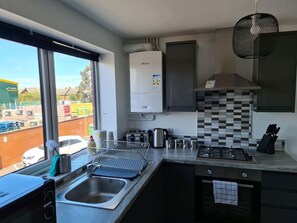 Cozinha moderna equipada com fogão a gás, forno embutido, micro-ondas e máquina de café. Uma janela oferece vista para o exterior.