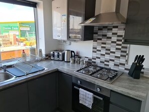 A kitchen with a gas stove, toaster, kettle, and a window with a view of a building. - Sav Apartments Nottingham Road Loughborough - 1Bed (Leicestershire)
