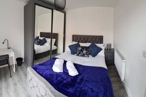 A hotel room with a bed, a desk, a chair, a radiator, and a mirror. - Sav Apartments Nottingham Road Loughborough - 1Bed (Leicestershire)