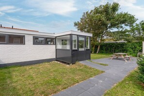 A modern house with a covered patio area, a small garden, and a picnic table. - Holiday apartment with 1 bedroom (Callantsoog)