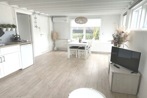 A bright kitchen with white cabinets, a dining table, and a TV on a stand. - Holiday apartment with 1 bedroom (Callantsoog)