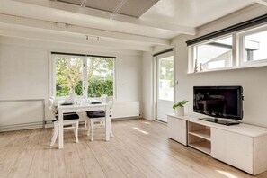 Eine moderne Küche mit Essbereich, einem Fernseher auf einem Holzschrank und großen Fenstern.