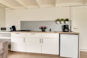 A compact kitchen with white cabinets, a microwave, a coffee maker, and a refrigerator. - Holiday apartment with 1 bedroom (Callantsoog)