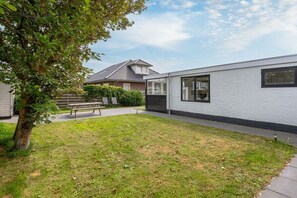 A modern building with a white exterior, a visible window, and a grassy yard with a tree. - Holiday apartment with 1 bedroom (Callantsoog)
