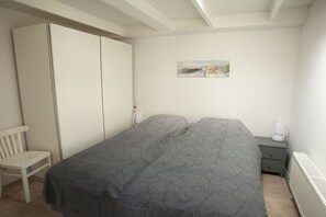 A bedroom with a bed, a chair, a wardrobe, a nightstand, and a painting on the wall. - Holiday apartment with 1 bedroom (Callantsoog)