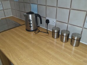 A kitchen counter with a kettle, a power strip, and three stainless steel containers. - Sav Apartments Pretoria Watford - 1 Bedroom (Hertfordshire)