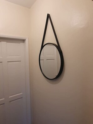 A white door with a black handle and a round mirror with a black frame hanging on the wall. - Sav Apartments Pretoria Watford - 1 Bedroom (Hertfordshire)