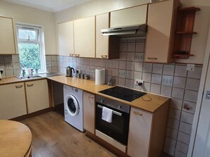 A compact kitchen with a washing machine, oven, and a small window. - Sav Apartments Pretoria Watford - 1 Bedroom (Hertfordshire)