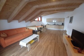 A spacious living area with a wooden ceiling, a sofa, a coffee table, a television, and a kitchen in the background. - Holiday apartment in Lana with swimming pool (Lana)