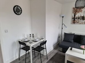 Een moderne woonruimte met een eettafel voor vier personen, een bank, een lamp en een klok aan de muur.