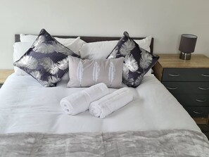 A neatly made bed with white linens, two rolled towels, and decorative pillows with a feather pattern. - Sav Apartments Nottingham Road Loughborough - 1Bed (Leicestershire)