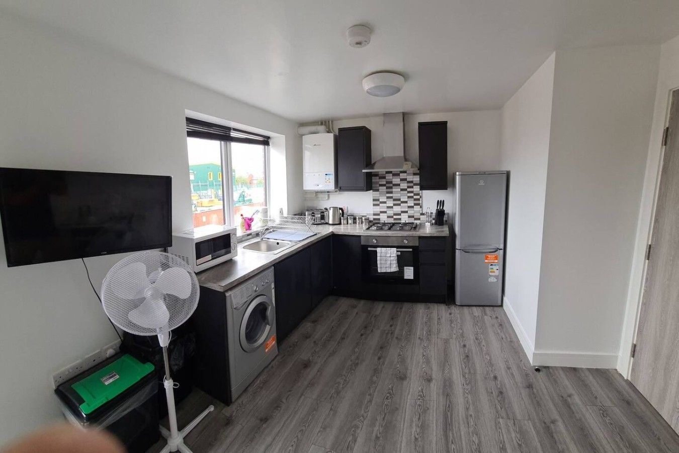 A compact kitchen with a washing machine, a microwave, a sink, a refrigerator, and a flat-screen TV.