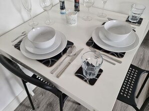 A dining table set with white plates, bowls, cutlery, and glasses, with black placemats and a decorative candle holder. - Sav Apartments Nottingham Road Loughborough - 1Bed (Leicestershire)