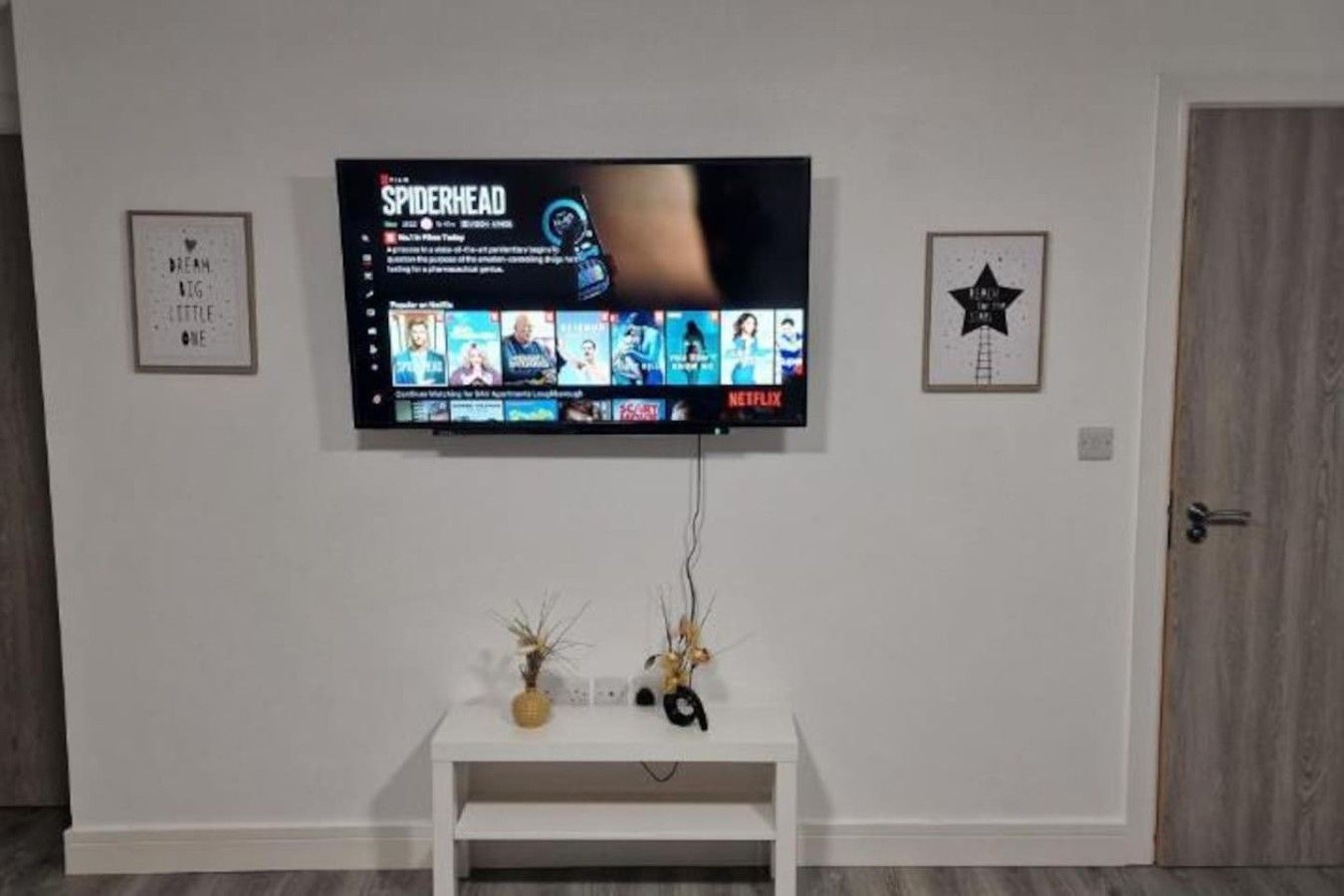 A television mounted on a wall with a white entertainment unit below it.