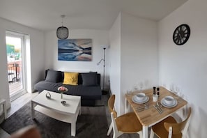 Ein gemütlicher Wohnbereich mit einer Couch, einem Esstisch für vier Personen, einem Couchtisch und einem Bild an der Wand.