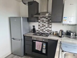 Eine kleine Küche mit Kühlschrank, Herd, Backofen und Spüle.