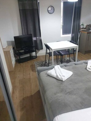 A hotel room with a bed, a TV, a small table with chairs, a clock on the wall, and a window with curtains. - SAV Regent Leicester: Luxury Studio Apartment (Leicester)