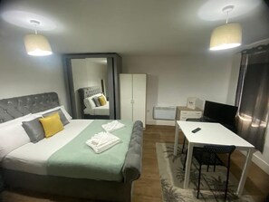 A hotel room with a bed, a desk, a chair, a wardrobe, and a television. - SAV Regent Leicester: Luxury Studio Apartment (Leicester)