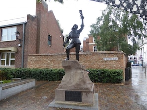 Een standbeeld van een historische figuur op een voetstuk, met een bakstenen muur en een bord waarop 'St. Martins East' staat.