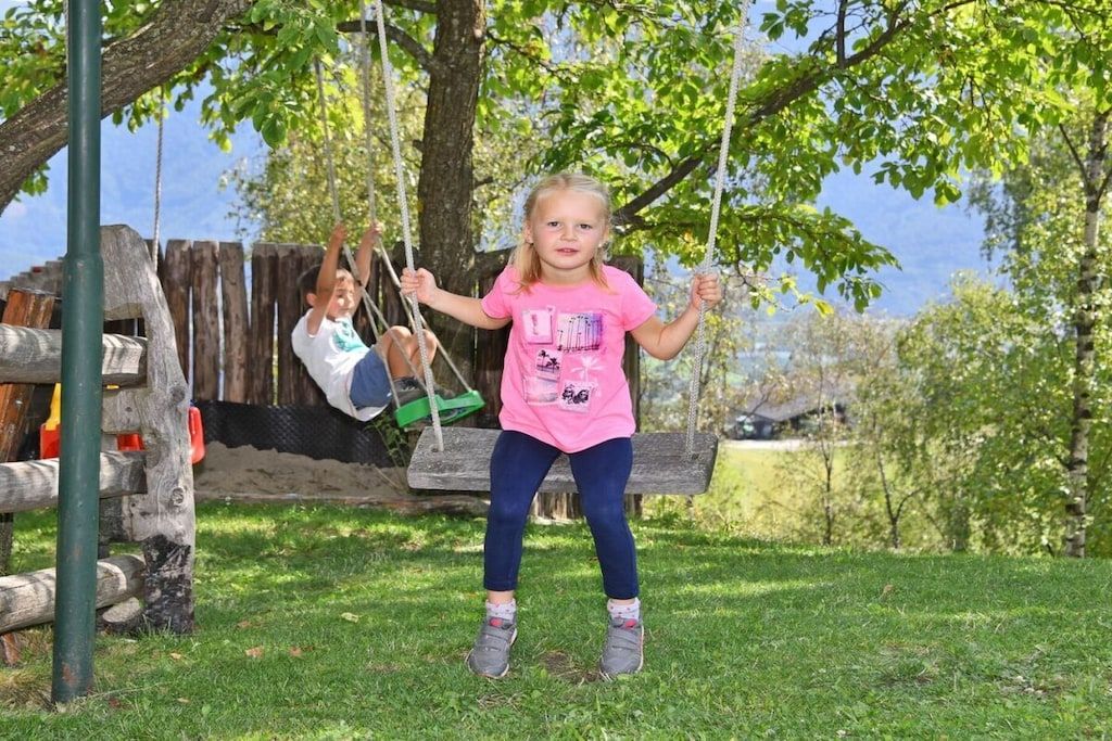 A child on a swing in a grassy area with trees in the background.
