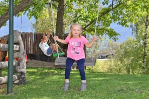 Ein Kind schaukelt in einer Wiese mit Bäumen im Hintergrund.
