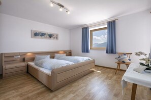 Ein Schlafzimmer mit einem Bett, Nachttischen, einem mit Vorhängen versehenen Fenster, einem Sessel und einem Tisch mit einer Pflanze.